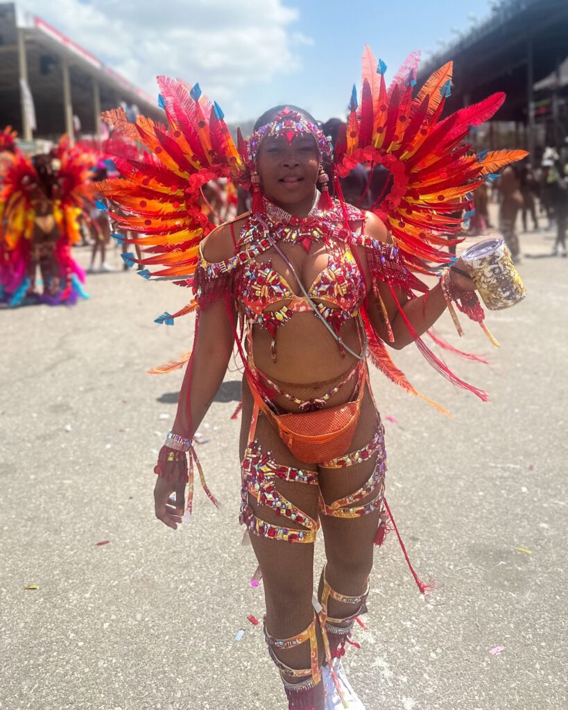 The author wears a costume inspired by the Chinese dragon. the costume features many feathers, gems and tassels of varied hues of red, orange, yellow, orange, and touches of blue.